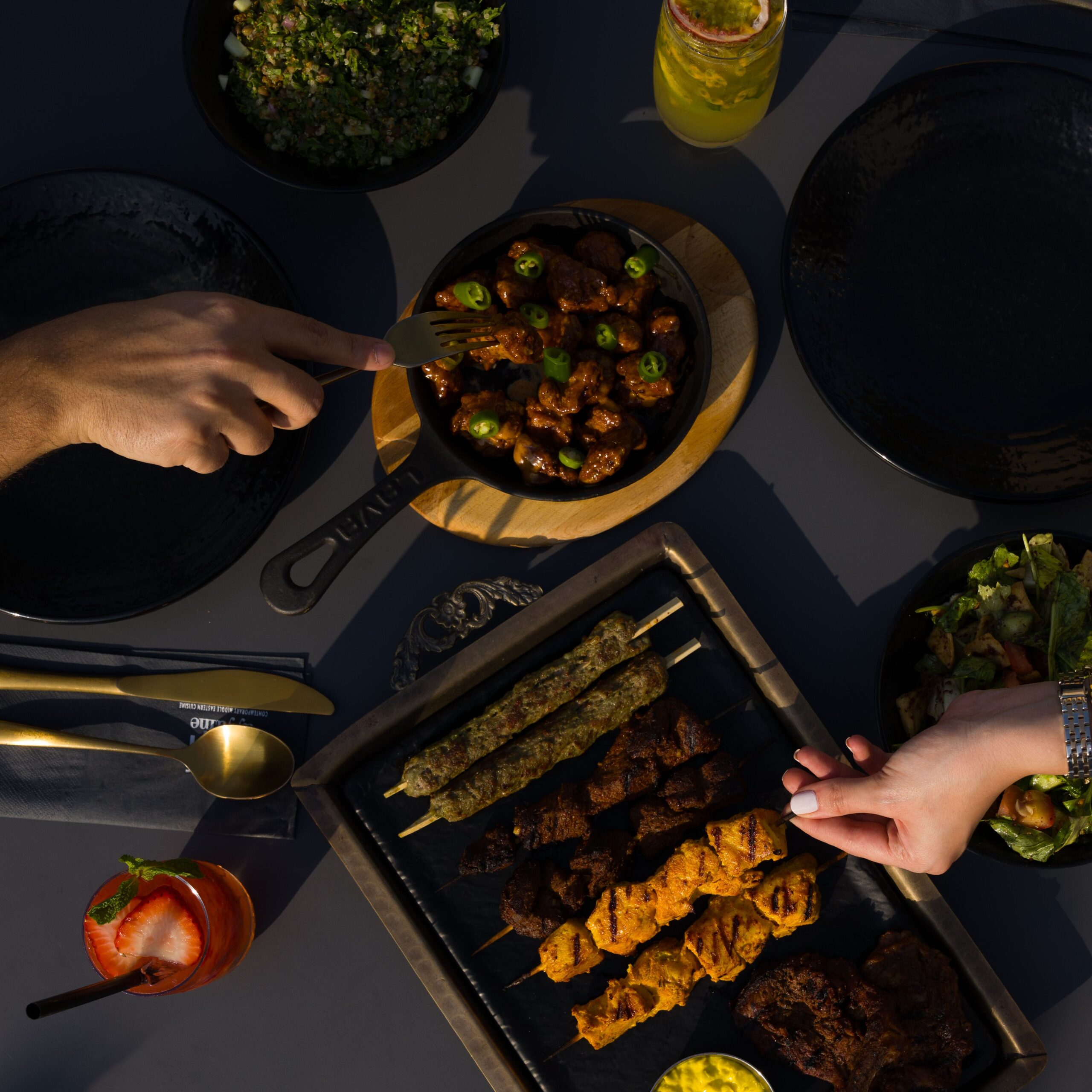 An outdoor dining setup featuring grilled skewers, salad, and refreshing drinks on a table.